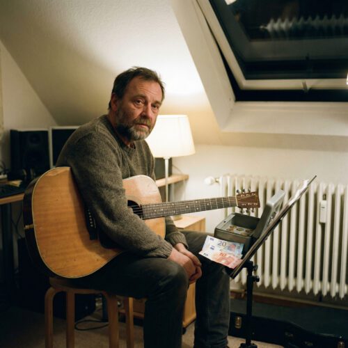 Erschöpfter Gitarrenlehrer blickt auf eine spärlich gefüllte Geldkassette auf einem Notenständer.